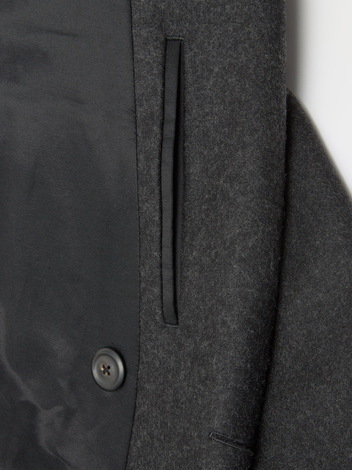 Close up of the dark grey oat with welt pocket inside and button closure detail