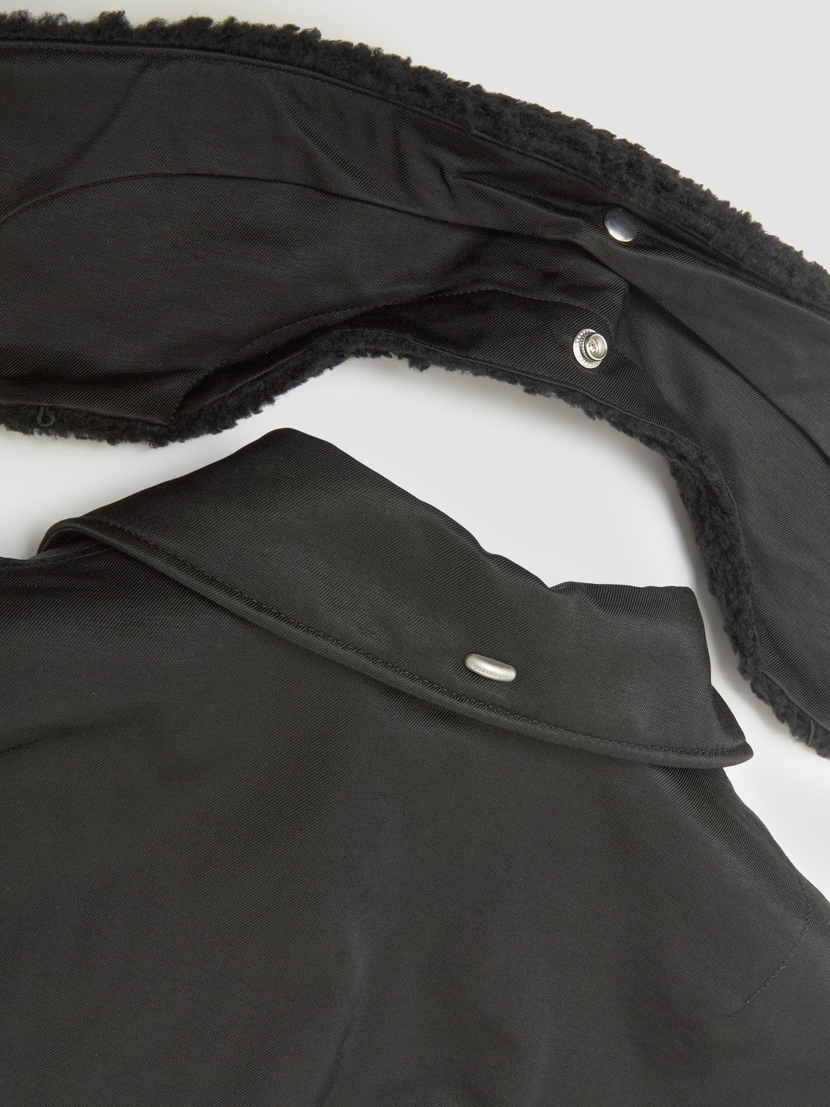 Close-up of a black coat with textured collar and buttons on a white background