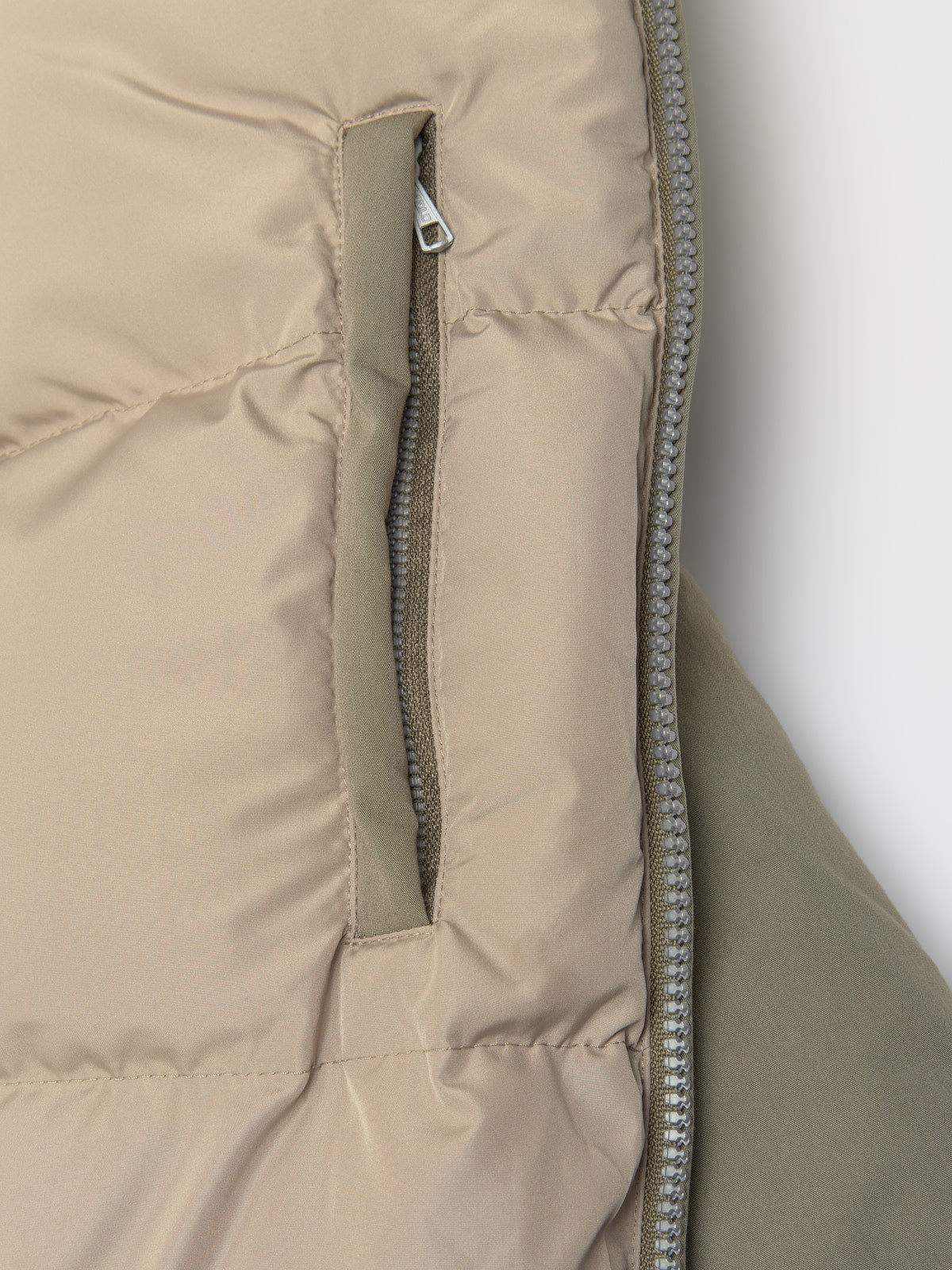 Close-up of a beige puffer jacket liner with a zipper on a white background