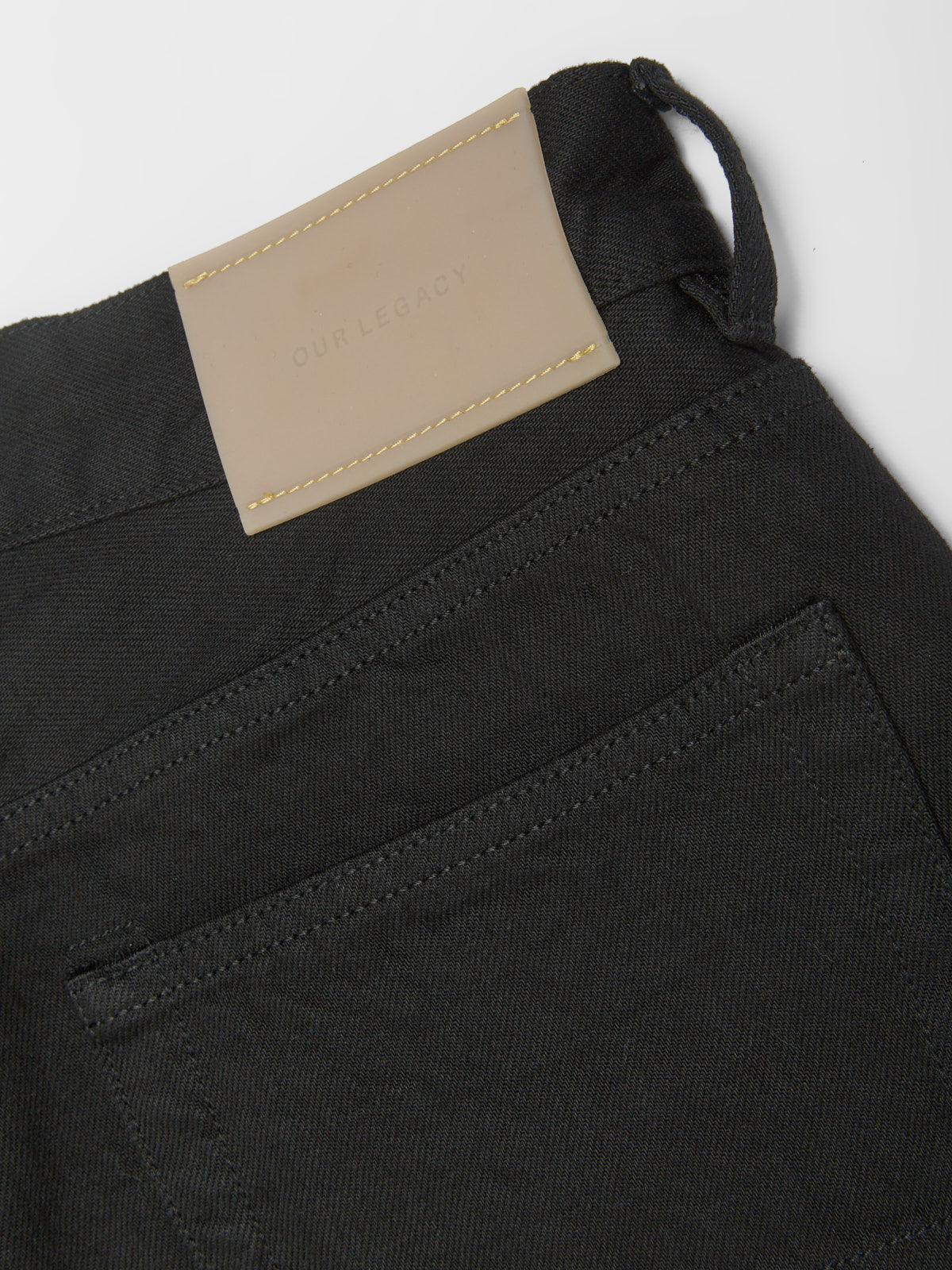 Close-up of black pants with a beige label on a light grey background