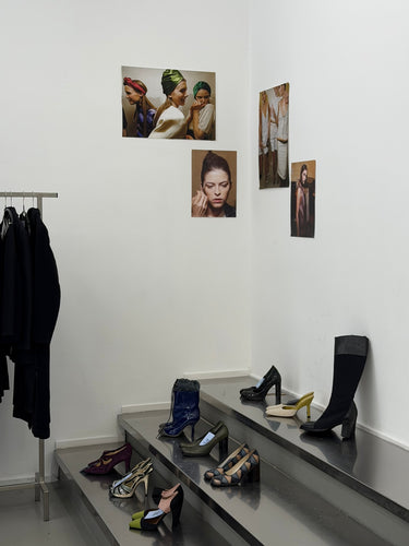 Shoe rack with various shoes on a platform, wall with framed pictures, and coat rack against a white wall.