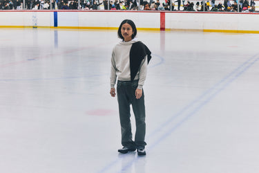 Person standing on an ice rink wearing a white sweater and dark pants.
