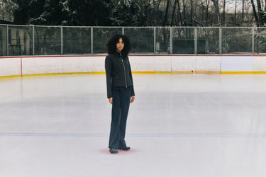 A person with dark jacket and pants standing on a ice rink.
