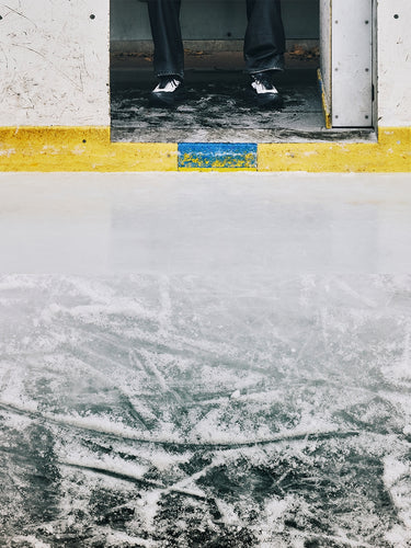 Person standing on a concrete surface with a yellow curb and blue paint in front of a ice rink.